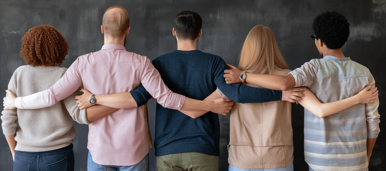 Personer står tillsammans med armarna runt varandra – symbol för lika rättigheter och inkludering enligt diskrimineringslagen.